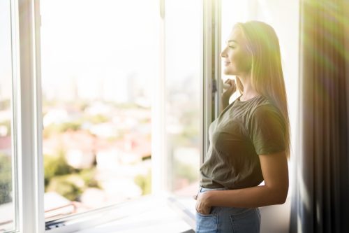 Person standing inside next to an open casement window and looking outside.